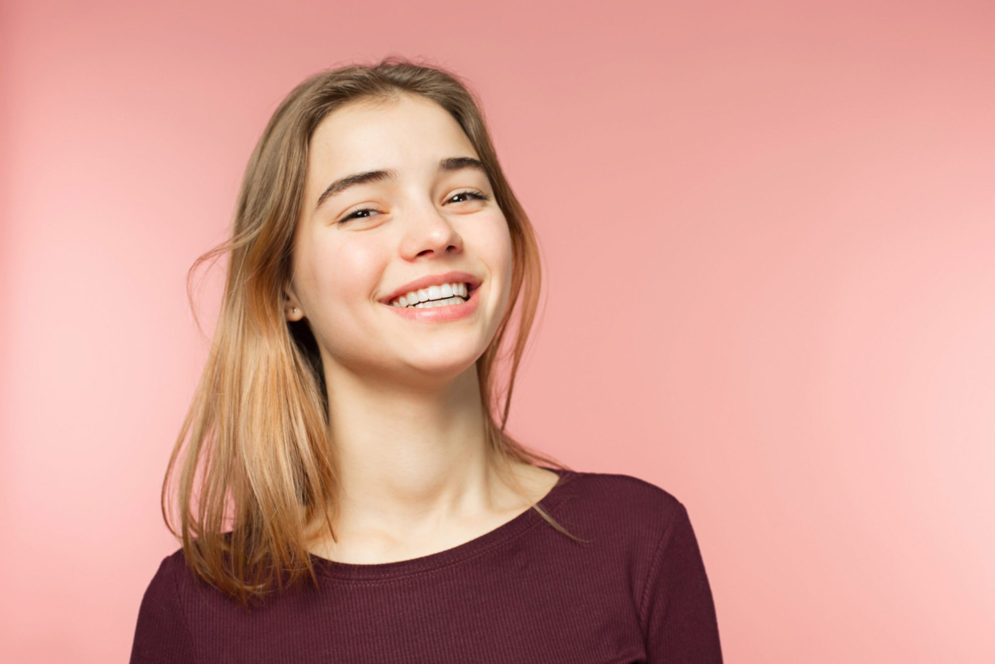 Woman smiling with perfect smile and white teeth on the pink studio background and looking at camera invisalign owensboro
